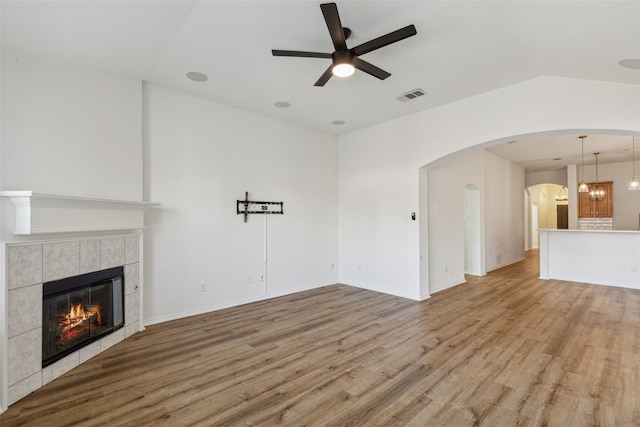 unfurnished living room with ceiling fan with notable chandelier, a tile fireplace, and light hardwood / wood-style flooring