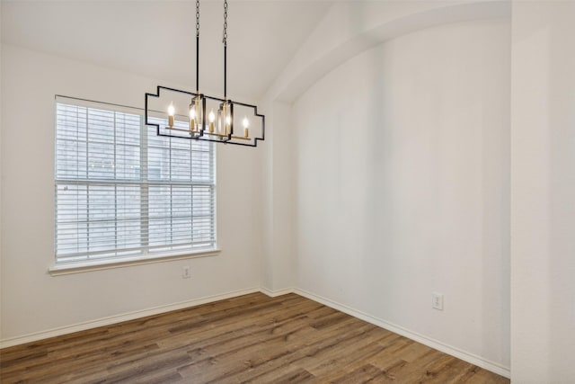 empty room with plenty of natural light, wood-type flooring, and a chandelier