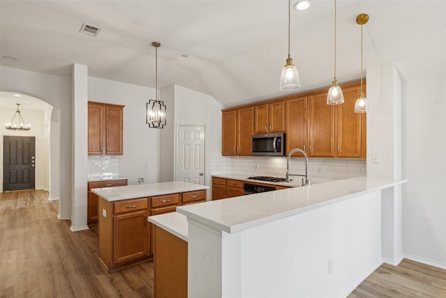 kitchen featuring a center island, backsplash, hanging light fixtures, light hardwood / wood-style flooring, and kitchen peninsula