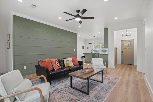 living room with light hardwood / wood-style flooring, ceiling fan with notable chandelier, and ornamental molding