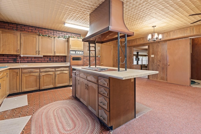 kitchen featuring island range hood, stainless steel gas cooktop, pendant lighting, a kitchen island, and wood walls