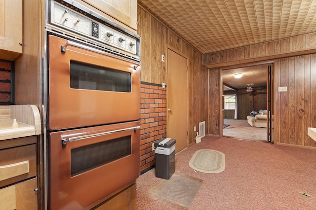 kitchen with wooden walls, double wall oven, and light carpet