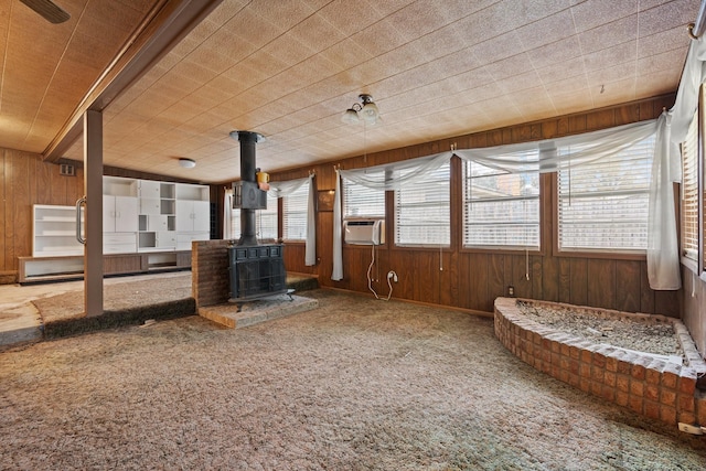 unfurnished living room featuring carpet flooring, a wood stove, wooden walls, and plenty of natural light