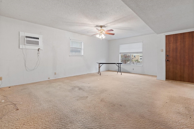 empty room featuring an AC wall unit, ceiling fan, light colored carpet, and a textured ceiling