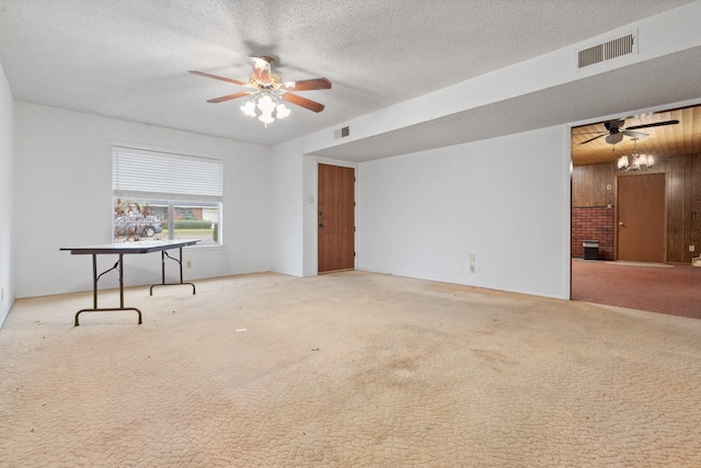 empty room featuring carpet flooring, ceiling fan, wood walls, and a textured ceiling