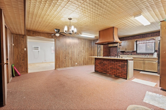 kitchen featuring hanging light fixtures, light carpet, wooden walls, custom range hood, and ceiling fan with notable chandelier