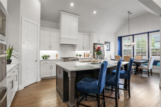 kitchen featuring stainless steel appliances, a kitchen island with sink, pendant lighting, and white cabinets