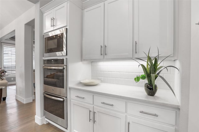 kitchen with built in microwave, white cabinetry, wood-type flooring, decorative backsplash, and stainless steel double oven