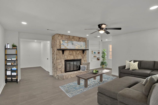 living room featuring ceiling fan, a stone fireplace, and wood-type flooring