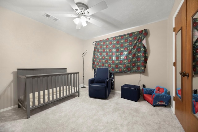 bedroom with a nursery area, carpet floors, and ceiling fan