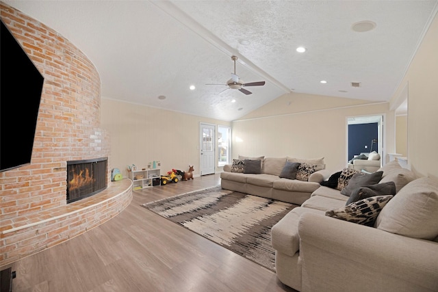 living room featuring a brick fireplace, a textured ceiling, vaulted ceiling, ceiling fan, and wood-type flooring