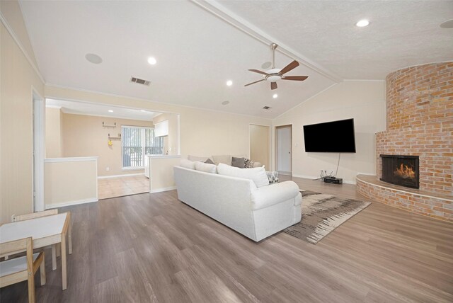 living room with vaulted ceiling with beams, ceiling fan, wood-type flooring, and a brick fireplace