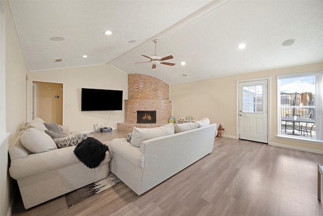 living room featuring lofted ceiling with beams, light hardwood / wood-style floors, a fireplace, and ceiling fan