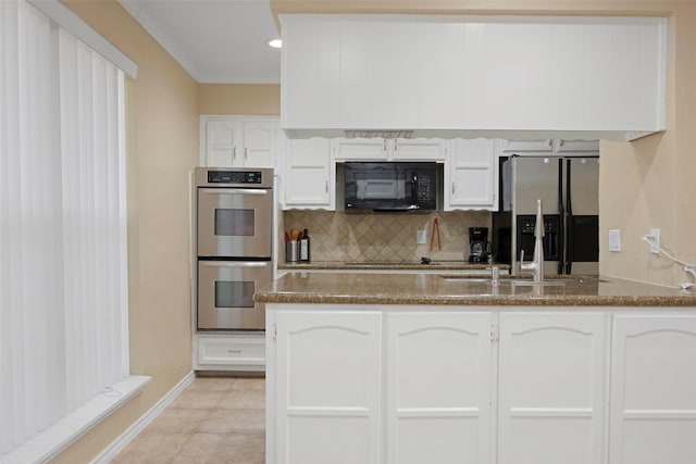 kitchen with dark stone counters, black appliances, sink, light tile patterned flooring, and white cabinetry