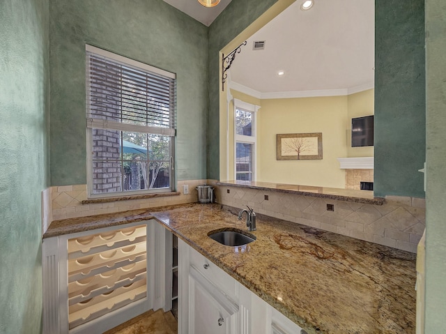 kitchen with white cabinets, light stone counters, ornamental molding, and sink