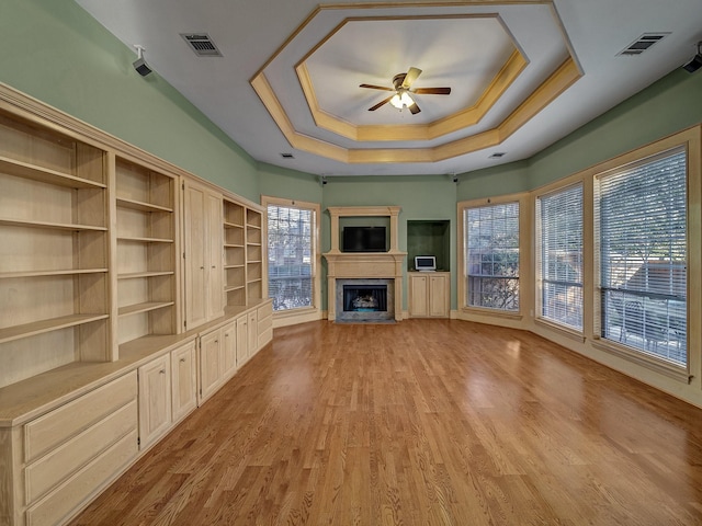 unfurnished living room featuring ceiling fan, a healthy amount of sunlight, a raised ceiling, and light wood-type flooring