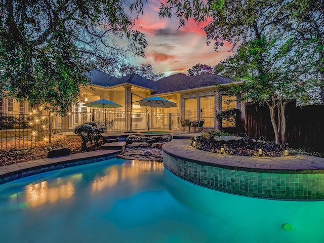 pool at dusk with a hot tub