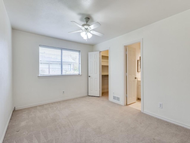 unfurnished bedroom featuring ensuite bathroom, light colored carpet, ceiling fan, a spacious closet, and a closet