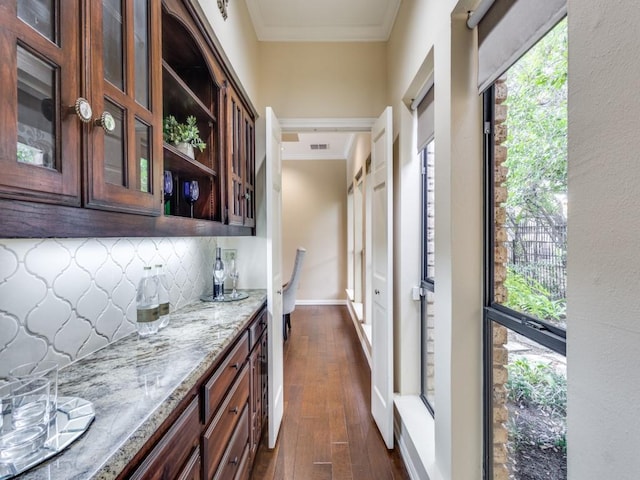 bar with decorative backsplash, light stone countertops, dark hardwood / wood-style flooring, and ornamental molding