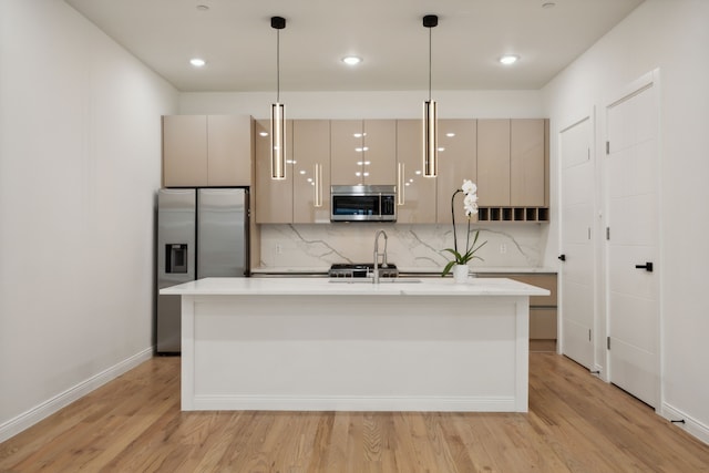 kitchen with hanging light fixtures, light wood-type flooring, a kitchen island with sink, backsplash, and appliances with stainless steel finishes