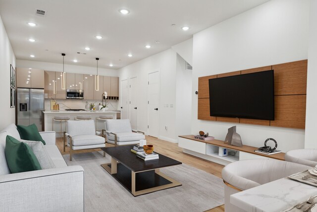 kitchen with hanging light fixtures, stainless steel appliances, an island with sink, light hardwood / wood-style floors, and sink