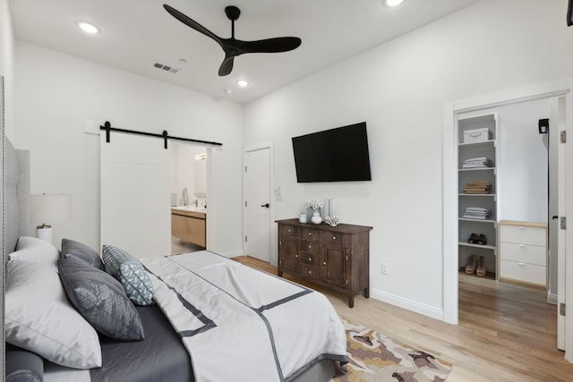 bedroom with ensuite bath, light wood-type flooring, ceiling fan, and a barn door