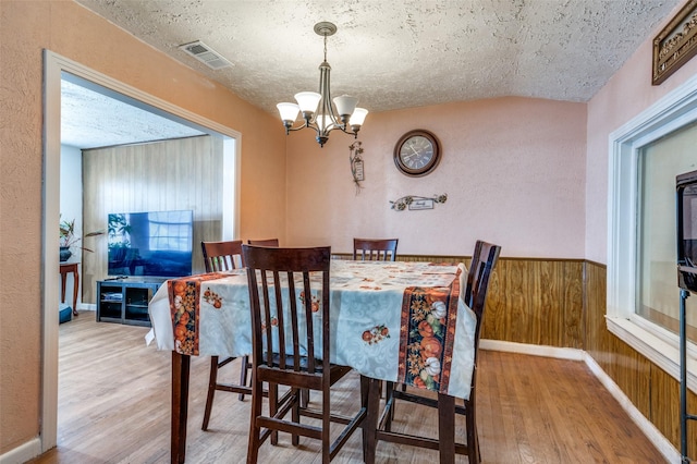 dining space with a notable chandelier, wood-type flooring, a textured ceiling, and wood walls