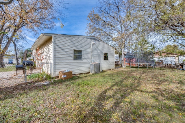 view of side of property with central AC unit, a yard, and a trampoline