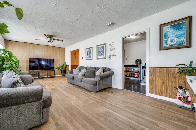 living room with hardwood / wood-style flooring, ceiling fan, a textured ceiling, and wood walls