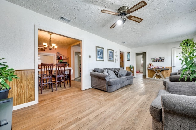 living room featuring wooden walls, ceiling fan with notable chandelier, a textured ceiling, and light hardwood / wood-style floors