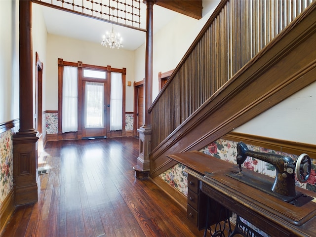 entrance foyer with dark hardwood / wood-style floors, ornate columns, and a notable chandelier