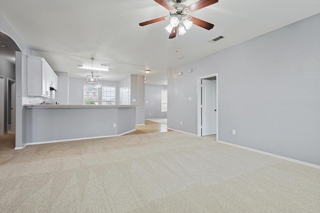 unfurnished living room featuring light colored carpet and ceiling fan with notable chandelier