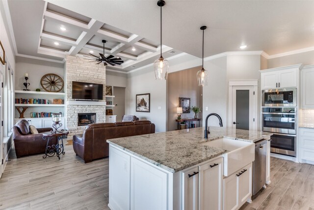 kitchen with coffered ceiling, stainless steel appliances, a kitchen island with sink, sink, and white cabinets