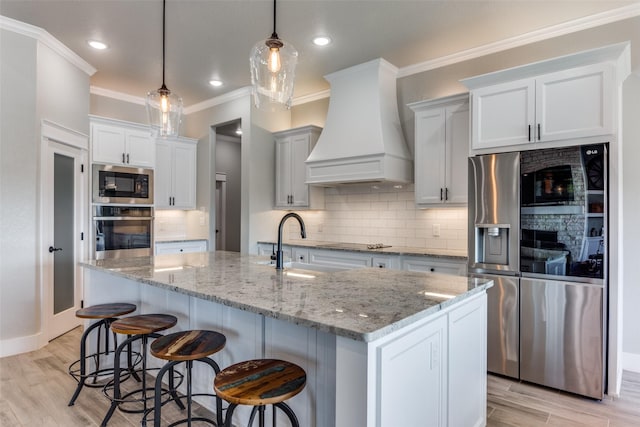 kitchen featuring white cabinetry, decorative light fixtures, a center island with sink, custom range hood, and appliances with stainless steel finishes