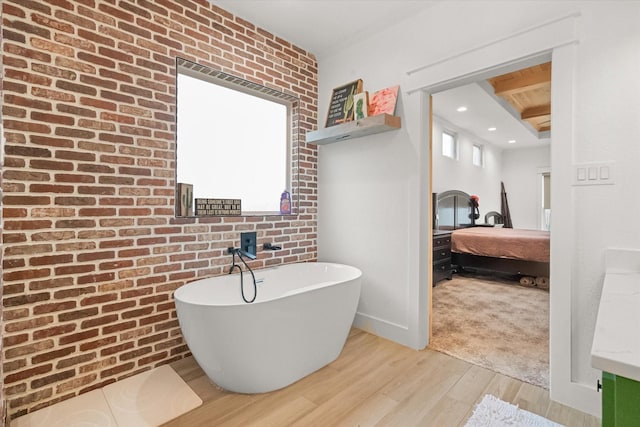 bathroom with a washtub, hardwood / wood-style flooring, and brick wall