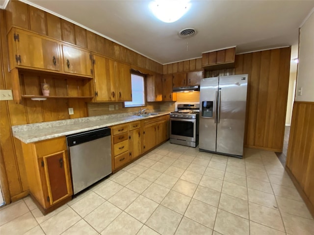 kitchen with sink, wood walls, crown molding, light tile patterned flooring, and appliances with stainless steel finishes