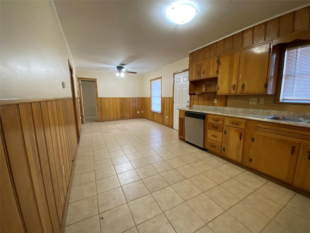 kitchen featuring ceiling fan, wooden walls, sink, light tile patterned floors, and dishwasher