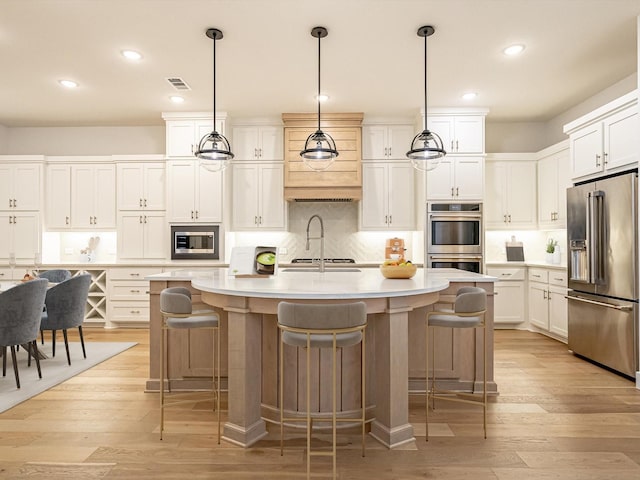 kitchen with double oven, pendant lighting, an island with sink, and white cabinets