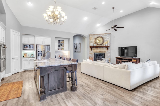 kitchen featuring appliances with stainless steel finishes, high vaulted ceiling, a fireplace, sink, and light hardwood / wood-style floors