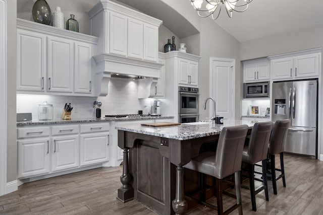 kitchen with light hardwood / wood-style flooring, appliances with stainless steel finishes, white cabinetry, tasteful backsplash, and a center island with sink