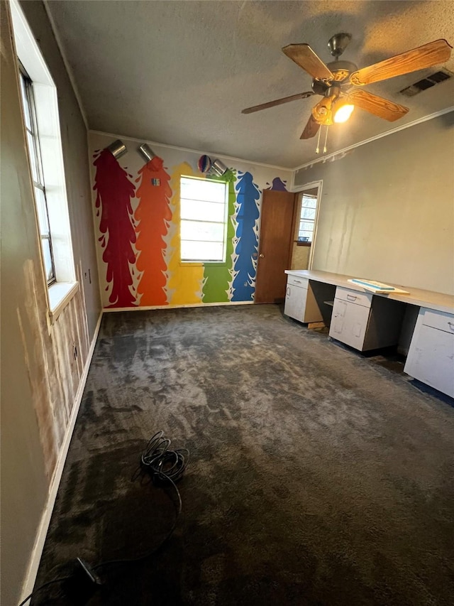 interior space featuring ceiling fan, dark carpet, built in desk, and ornamental molding