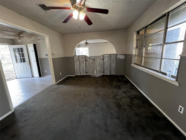 spare room featuring ceiling fan, a healthy amount of sunlight, a textured ceiling, and dark carpet