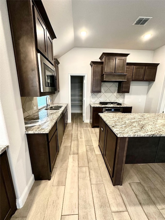 kitchen with sink, dark brown cabinetry, stainless steel appliances, light stone countertops, and light hardwood / wood-style flooring