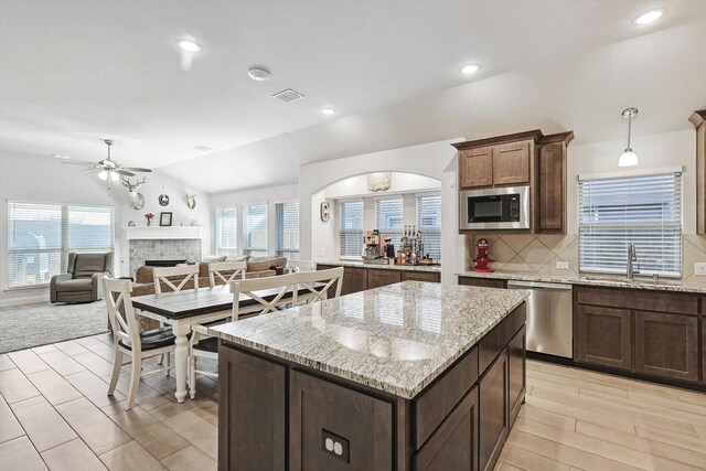 kitchen with vaulted ceiling, a kitchen island, a fireplace, stainless steel appliances, and light stone countertops