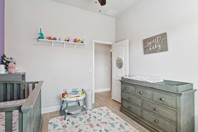 bedroom featuring lofted ceiling, a crib, light hardwood / wood-style floors, and ceiling fan