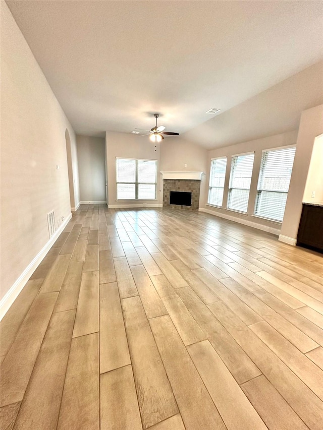 unfurnished living room featuring plenty of natural light, light hardwood / wood-style floors, a tile fireplace, and ceiling fan