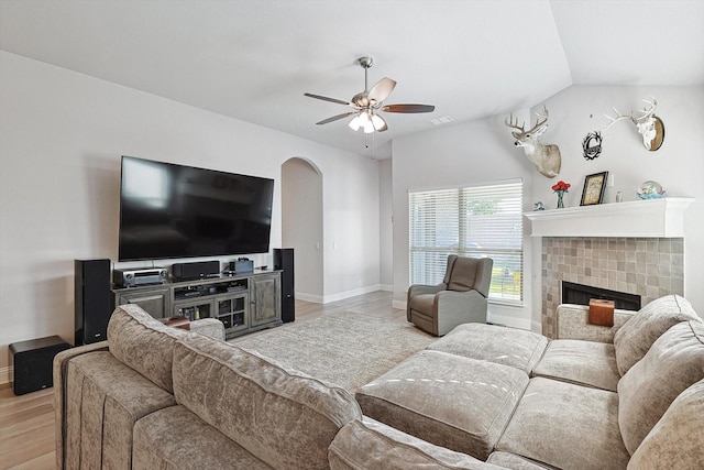 living room featuring ceiling fan, vaulted ceiling, a tile fireplace, and light wood-type flooring