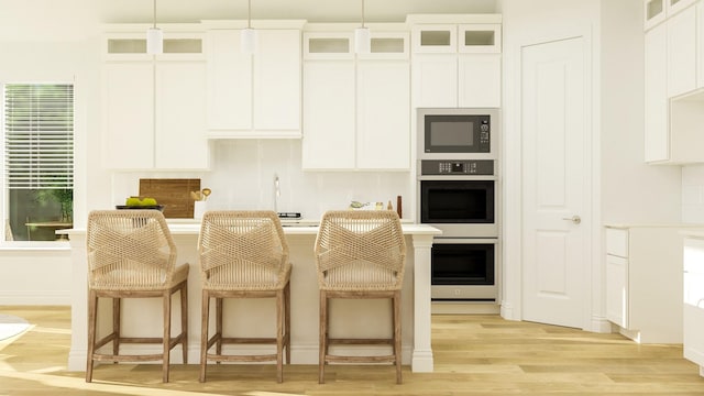 kitchen with white cabinetry, decorative light fixtures, black microwave, and light hardwood / wood-style flooring