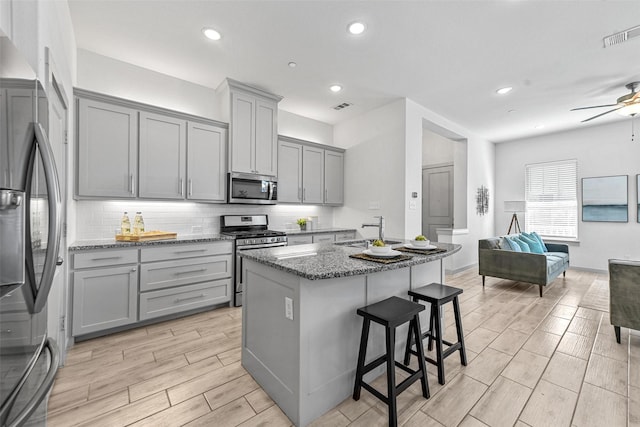 kitchen featuring appliances with stainless steel finishes, gray cabinets, a breakfast bar area, and dark stone counters