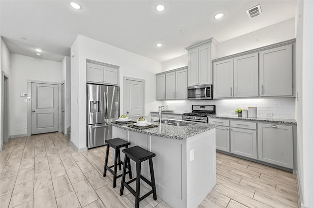 kitchen featuring light stone counters, sink, a center island with sink, and appliances with stainless steel finishes